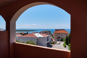 A view through an archway of a coastal area with buildings and a clear sky. - Comfortable Apartments Malina B4 br 4 (Novalja)