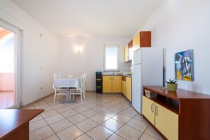 A kitchen with yellow cabinets, a white refrigerator, and a dining table with chairs. - Comfortable Apartments Malina B4 br 4 (Novalja)