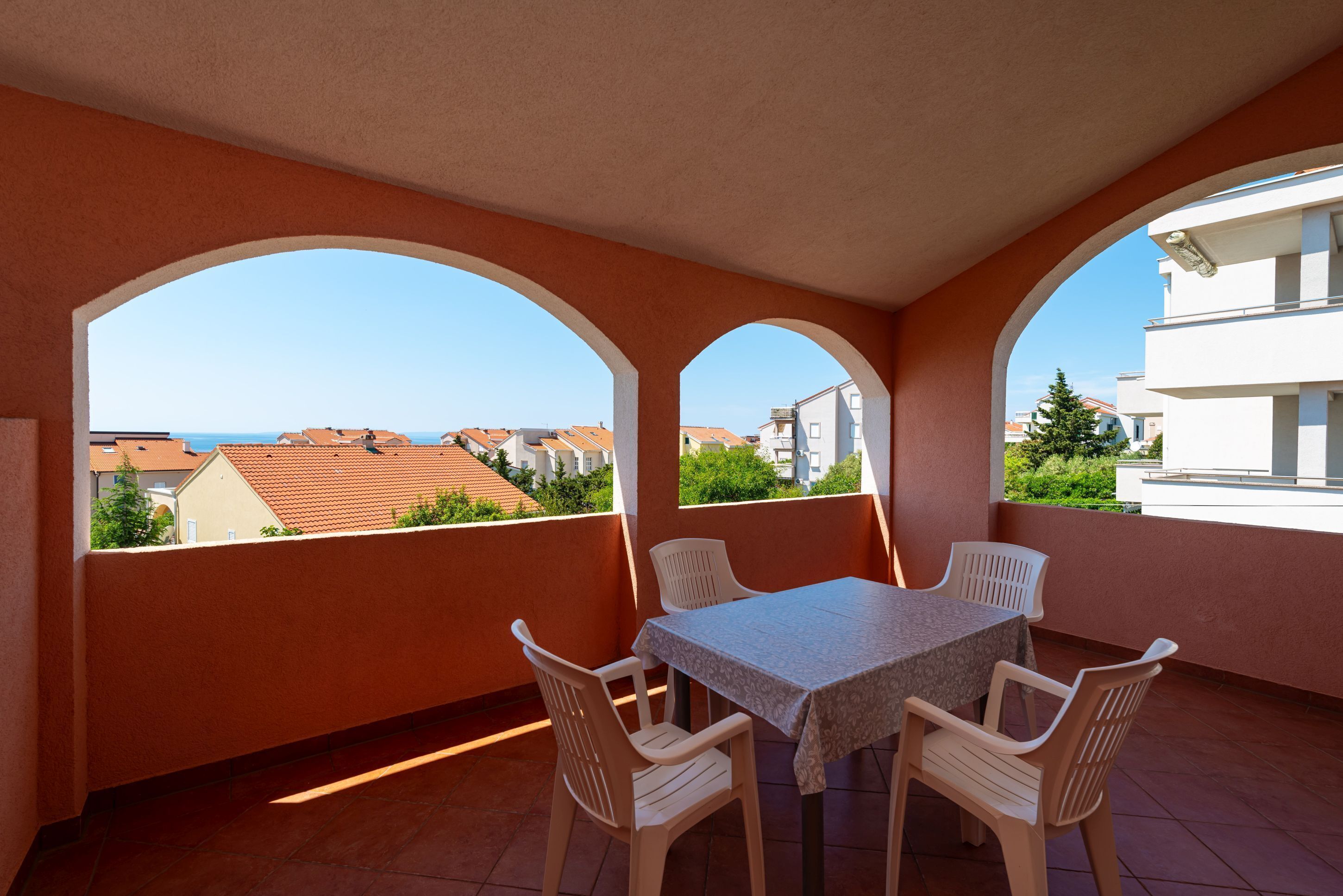 A balcony with a table and chairs, a view of buildings, and a clear sky.
