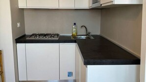 Een kleine keuken met witte kastjes, een zwart aanrecht, een gasfornuis en een roestvrijstalen spoelbak.