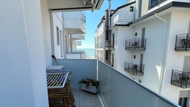 Een smal balkon met een tafel en stoelen, een plant in pot en uitzicht op zee.