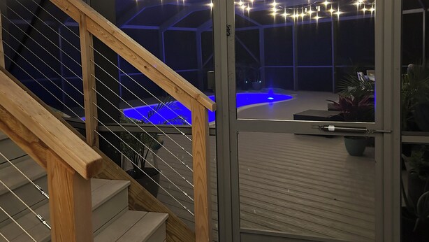 A modern interior with a wooden staircase, a glass door leading to a pool area, and string lights. - Treetop getaway on a secluded Island with gulf coast beaches  (Captiva)