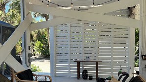 A covered outdoor seating area with wicker furniture, a ceiling fan, string lights, and a view through a white lattice screen. - Treetop getaway on a secluded Island with gulf coast beaches  (Captiva)