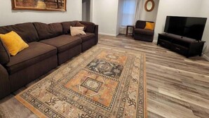 Ein Wohnzimmer mit einem braunen Sofa, einem gemusterten Teppich, einem Fernseher und einem Bild an der Wand.