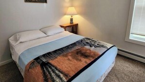 Ein Schlafzimmer mit Bett, Nachttisch mit Lampe, einem Bild an der Wand und einem Fenster mit Jalousien.