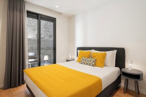 A modern hotel room with a large bed, a view through a glass door, and a small table with a lamp. - Golden City by An Island Apart (Funchal)