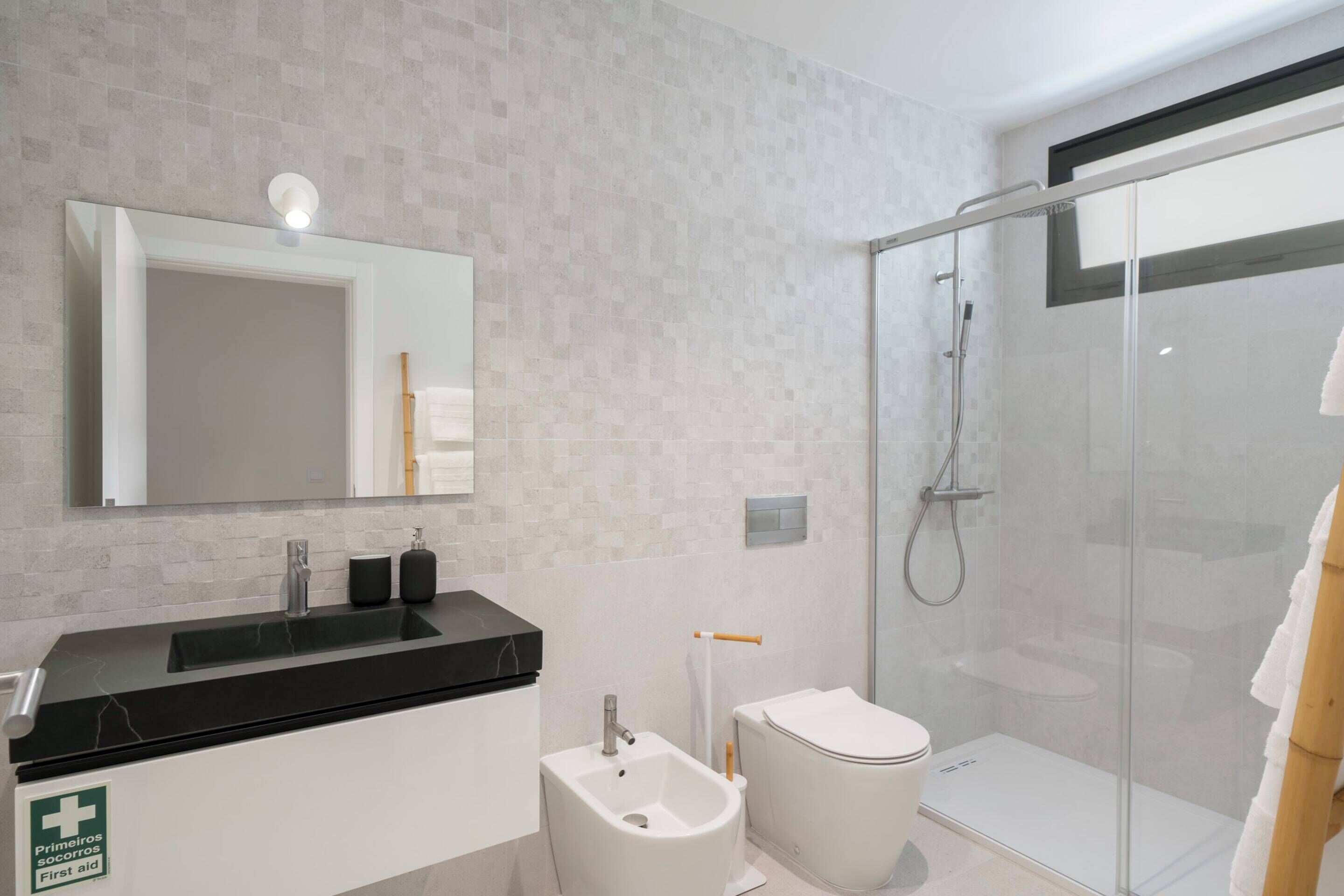 Ein modernes Badezimmer mit einem schwarzen Waschbecken, einem Bidet, einer Toilette und einer Duschkabine.