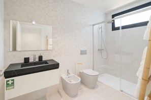 Features a sleek vanity, large mirror, bidet, and toilet, with a glass shower enclosure.