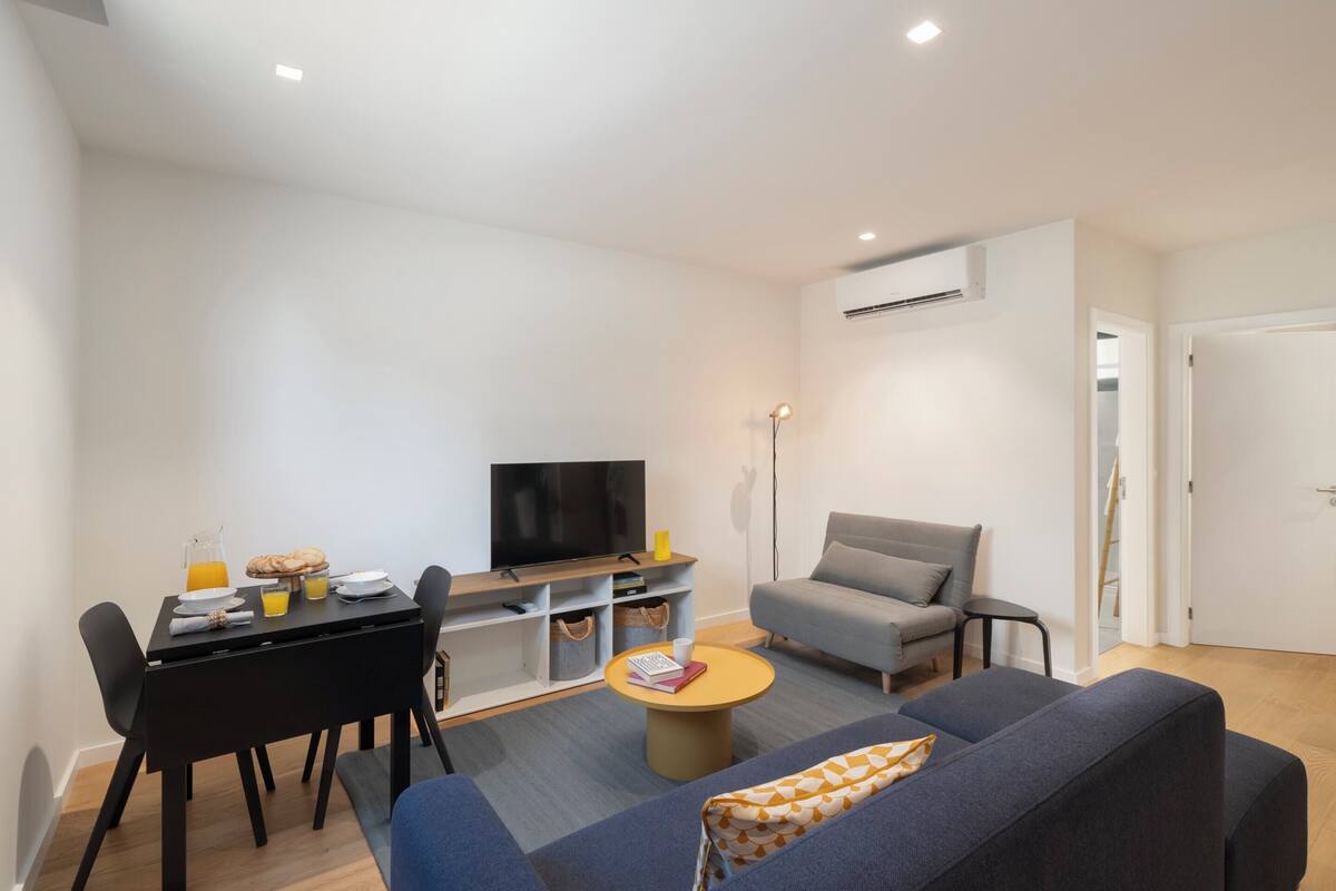 A modern living room with a sofa, a coffee table, a TV, and a dining area with chairs and a table.
