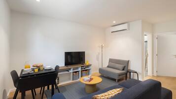 A modern living room with a sofa, a coffee table, a TV, and a dining area with chairs and a table.