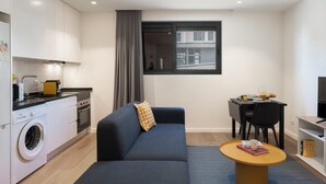 A modern kitchen with a washing machine, a dining area with a table and chairs, a sofa, and a TV. - Golden City by An Island Apart (Funchal)