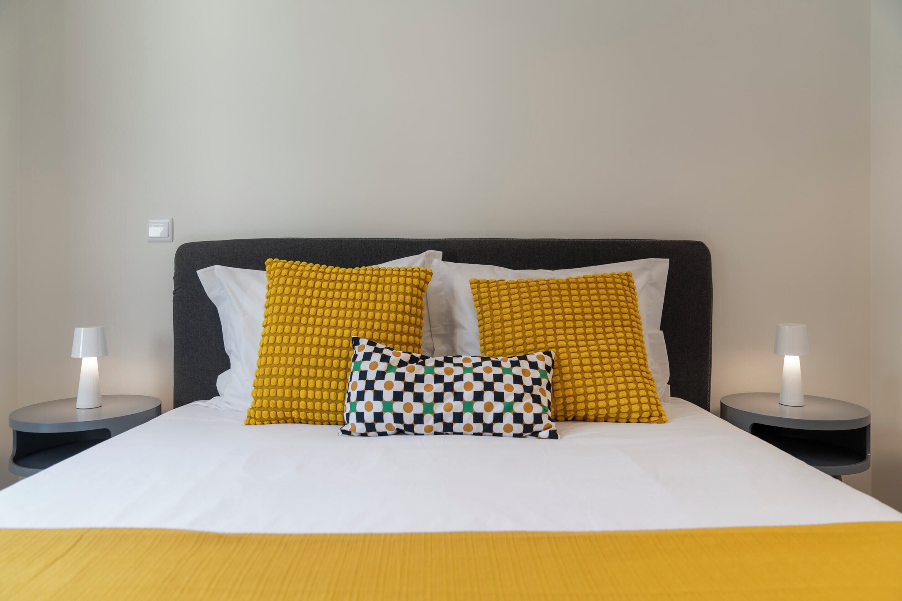 A neatly made bed with a white and yellow bedspread, two matching nightstands, and a checkered pillow.