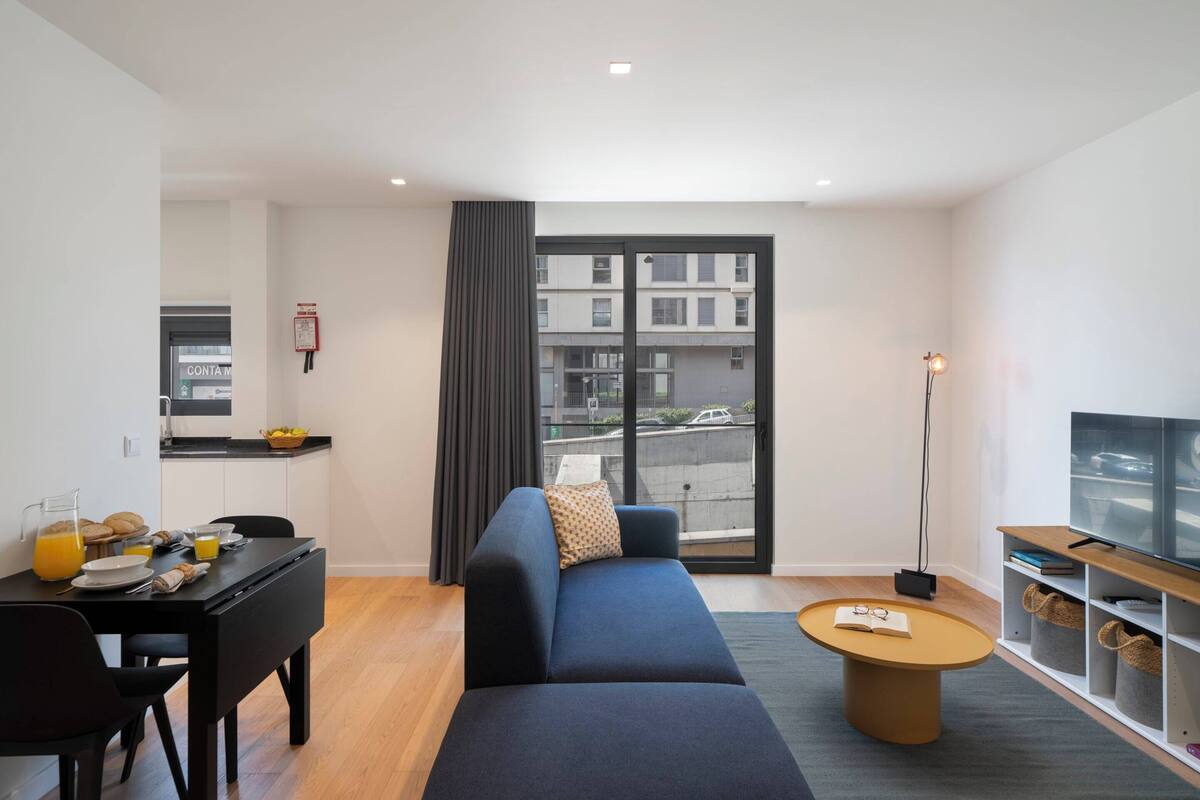A modern living room with a sofa, a coffee table, a TV stand, and a dining area with a table and chairs.