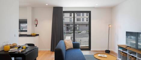 A modern living room with a sofa, a coffee table, a TV stand, and a dining area with a table and chairs.