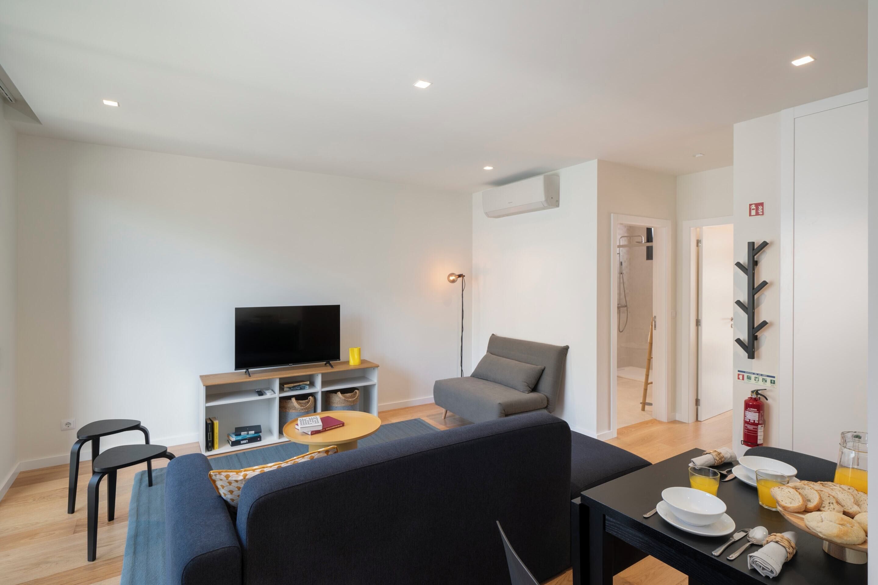 Een moderne woonkamer met een bank, een eettafel gedekt met borden en glazen, een flatscreen-tv en een klein bijzettafeltje.