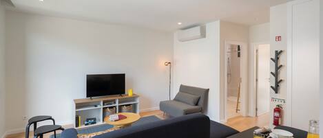 Een moderne woonkamer met een bank, een eettafel gedekt met borden en glazen, een flatscreen-tv en een klein bijzettafeltje.
