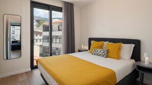A hotel room with a large bed, a nightstand, a mirror, and a view of the outside. - Golden City by An Island Apart (Funchal)