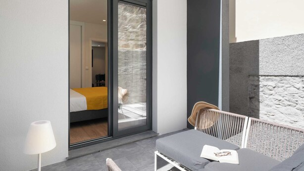 A modern room with a sliding glass door leading to a balcony, a bed with a yellow blanket, and a small table with a book. - Golden City by An Island Apart (Funchal)