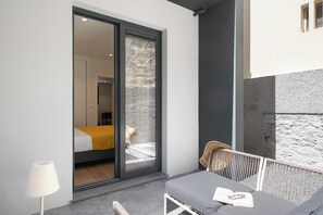 A modern room with a sliding glass door leading to a balcony, a bed with a yellow blanket, and a small table with a book. - Golden City by An Island Apart (Funchal)