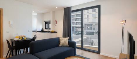 A modern living room with a sofa, a coffee table, and a view of a cityscape through large windows.