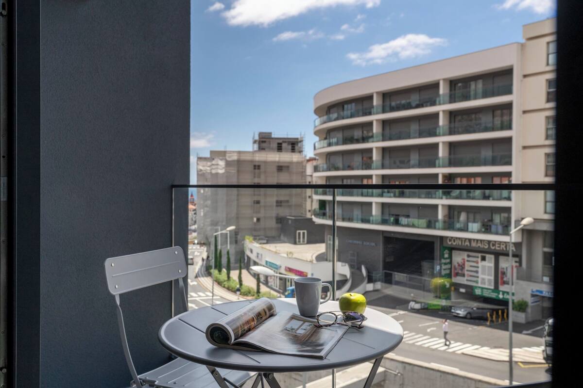 A balcony with a table, chair, and a view of a cityscape.