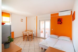 A hotel room with a bed, a dining table with chairs, a small kitchen area, and a sliding glass door to the outside. - Comfortable Apartments Malina A4 br 3 (Novalja)