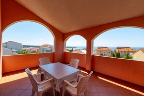 A balcony with a table and chairs, a view of the sea, and buildings in the background. - Comfortable Apartments Malina A4 br 3 (Novalja)