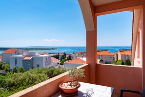A balcony with a potted plant, a table, and a clear view of a coastal town. - Comfortable Apartments Malina C6 br 8 (Novalja)