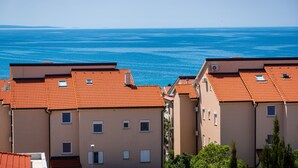 Ein Küstenwohngebiet mit Häusern mit Terrakotta-Dächern, blauem Meer und einer fernen Küstenlinie.