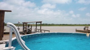 A swimming pool with a wooden deck, a lifeguard stand, and a view of the water. - Large Home Near the Caney Y with Pool! (Bay City)