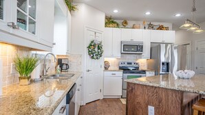 A modern kitchen with white cabinets, granite countertops, a wooden island, stainless steel appliances, and a decorative wreath. - Large Home Near the Caney Y with Pool! (Bay City)