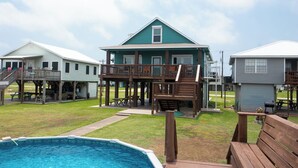 A pool area with a wooden deck, a covered seating area, and a building with a green roof and multiple decks. - Large Home Near the Caney Y with Pool! (Bay City)