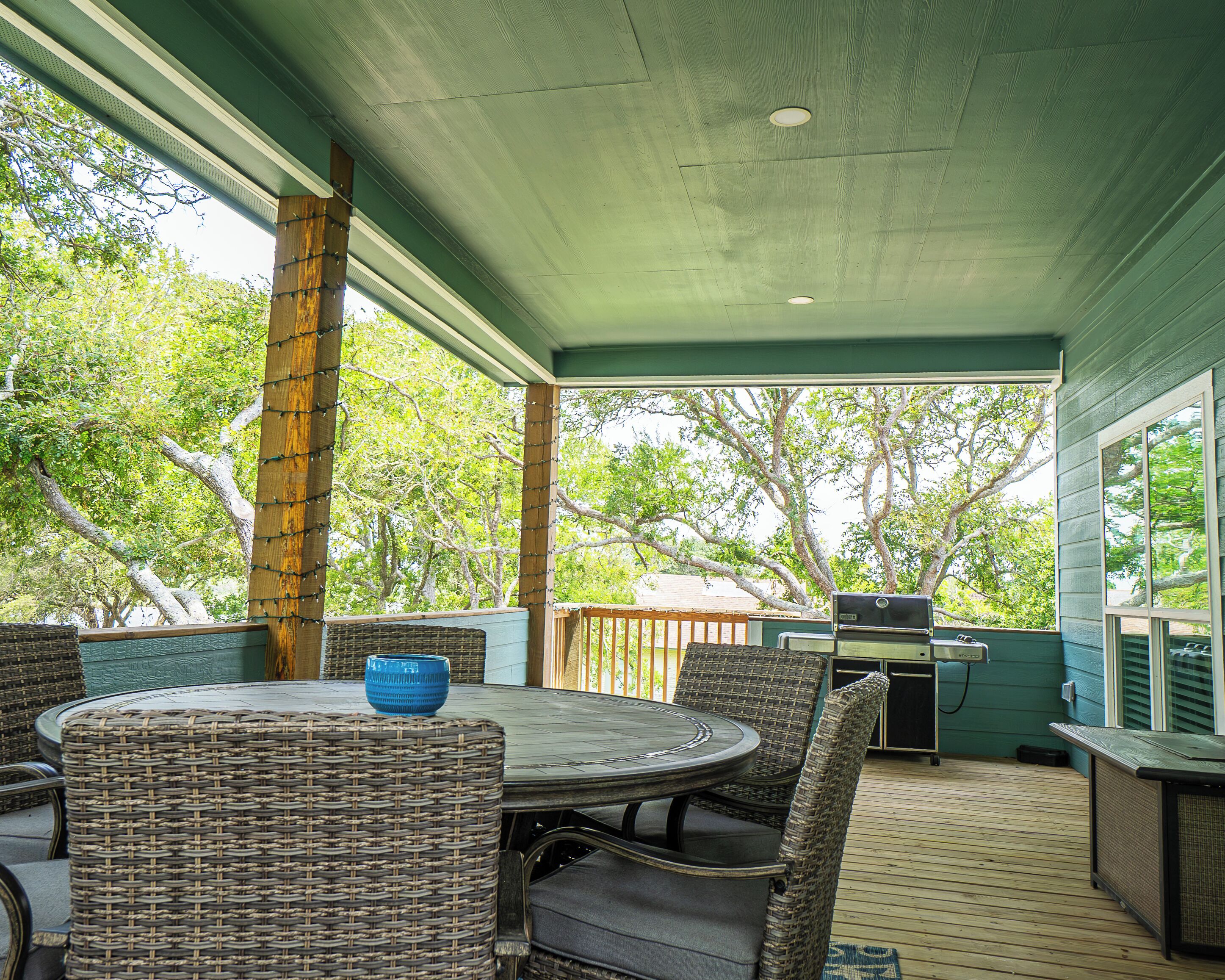 An outdoor patio with a round table, wicker chairs, and a grill.