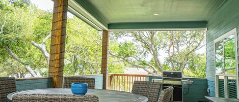 An outdoor patio with a round table, wicker chairs, and a grill.
