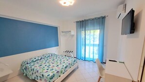 Un dormitorio con cama, escritorio, silla, televisor y ventana con cortinas.