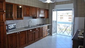 Una cocina con armarios de madera, encimera de granito, pileta de acero inoxidable y cocina a gas. Hay una puerta corrediza de vidrio que da a un balcón exterior con una mesa y sillas.