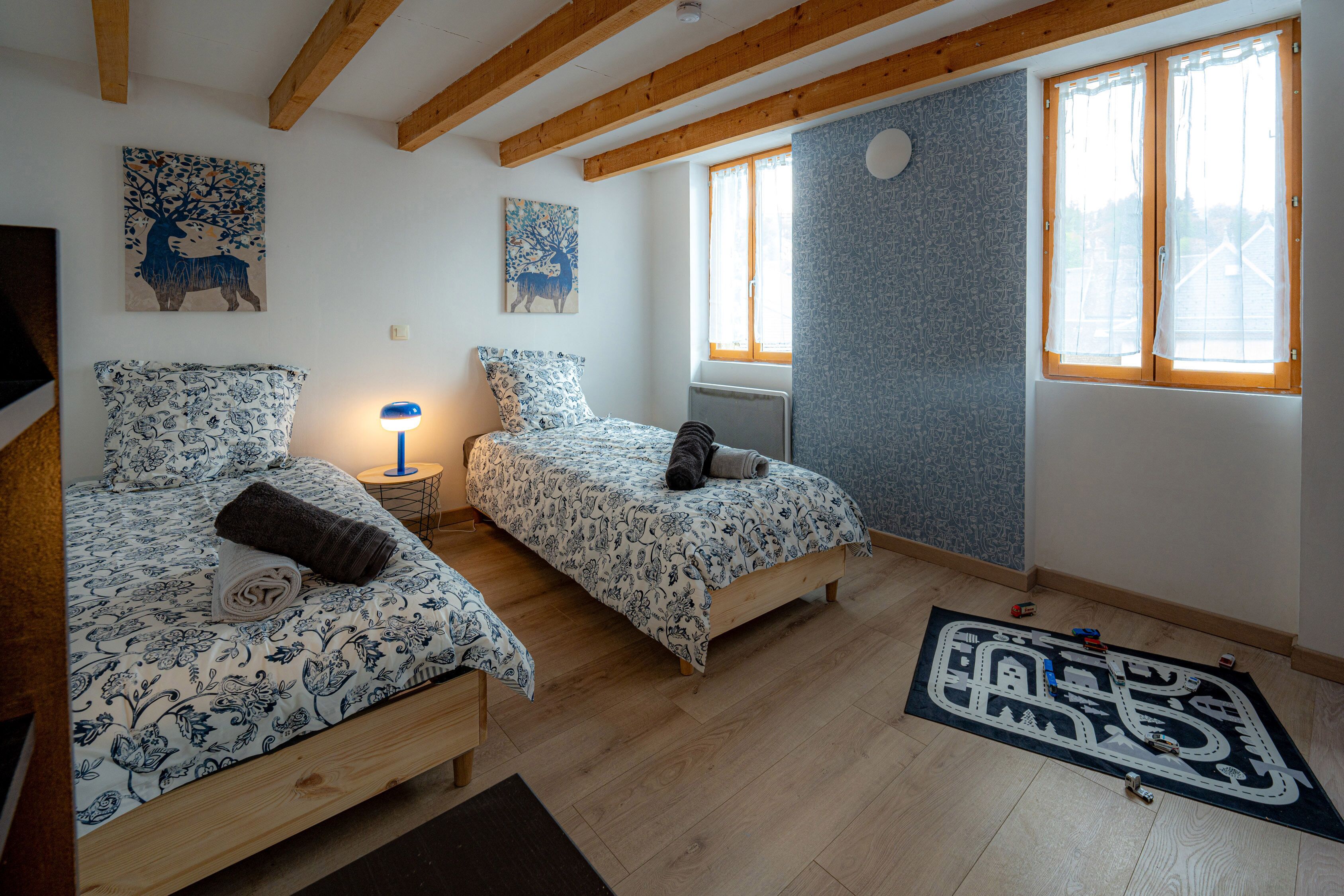 A bedroom with two beds, a nightstand, a lamp, and a window with curtains.