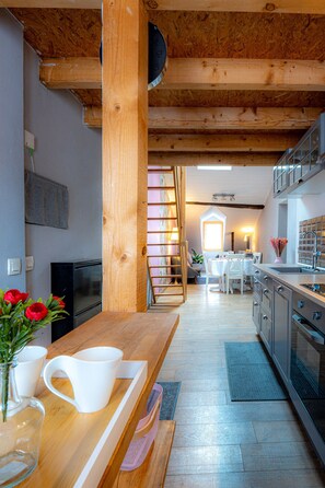 Een moderne keuken met houten balken, een eethoek met een witte tafel en stoelen, en uitzicht op een slaapkamer met een raam.
