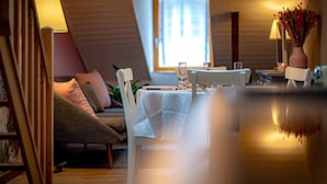 Un coin repas accueillant avec une table dressée pour deux personnes, un canapé confortable et une fenêtre laissant entrer la lumière naturelle.