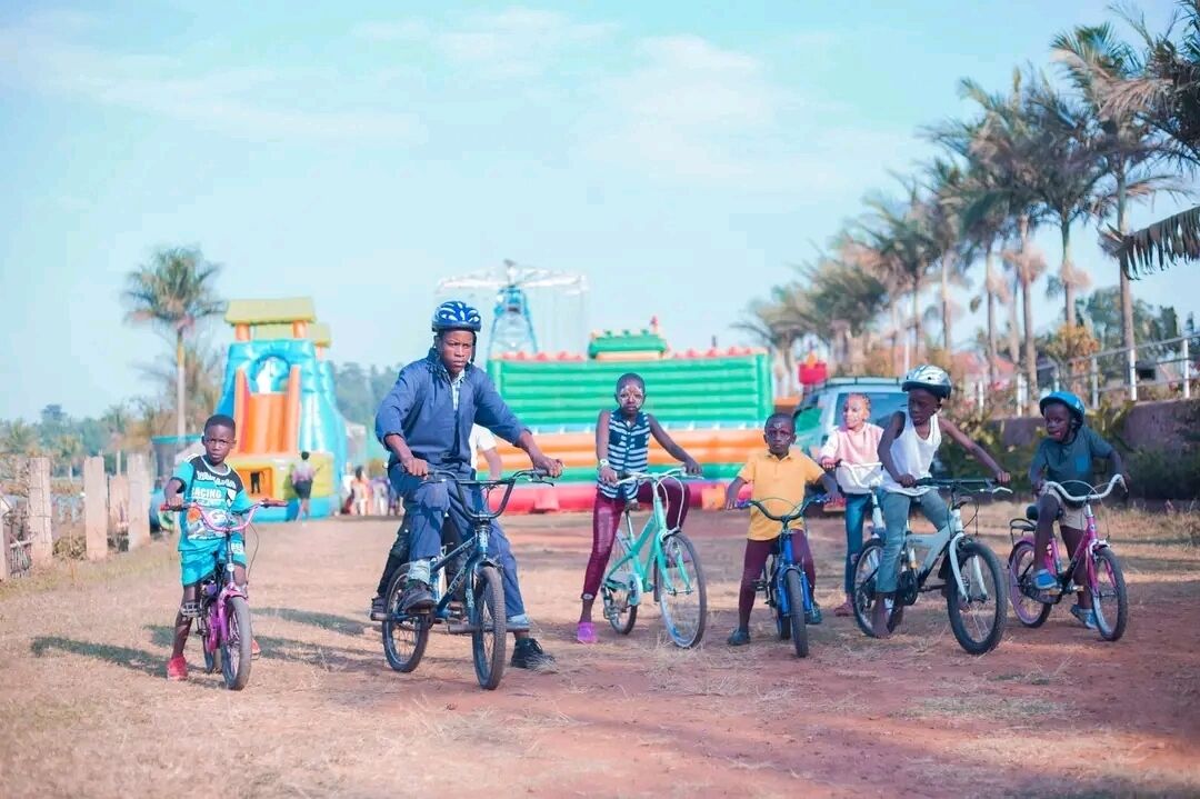 A group of people on bicycles in an outdoor setting with a playground and palm trees in the background.