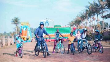A group of people on bicycles in an outdoor setting with a playground and palm trees in the background.