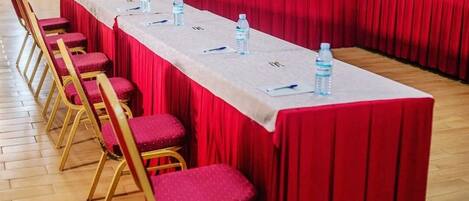 Une salle de conférence avec une longue table, des chaises rouges et des bouteilles d’eau posées sur la table.