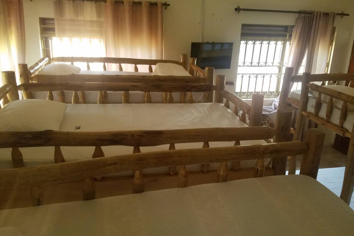 A room with two wooden bunk beds, a television on the wall, and a window with curtains.