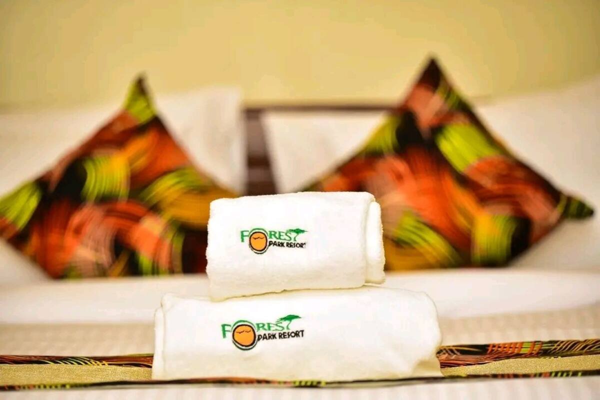 Two neatly folded towels with the logo of Forest Park Resort on a bed with colorful patterned pillows.