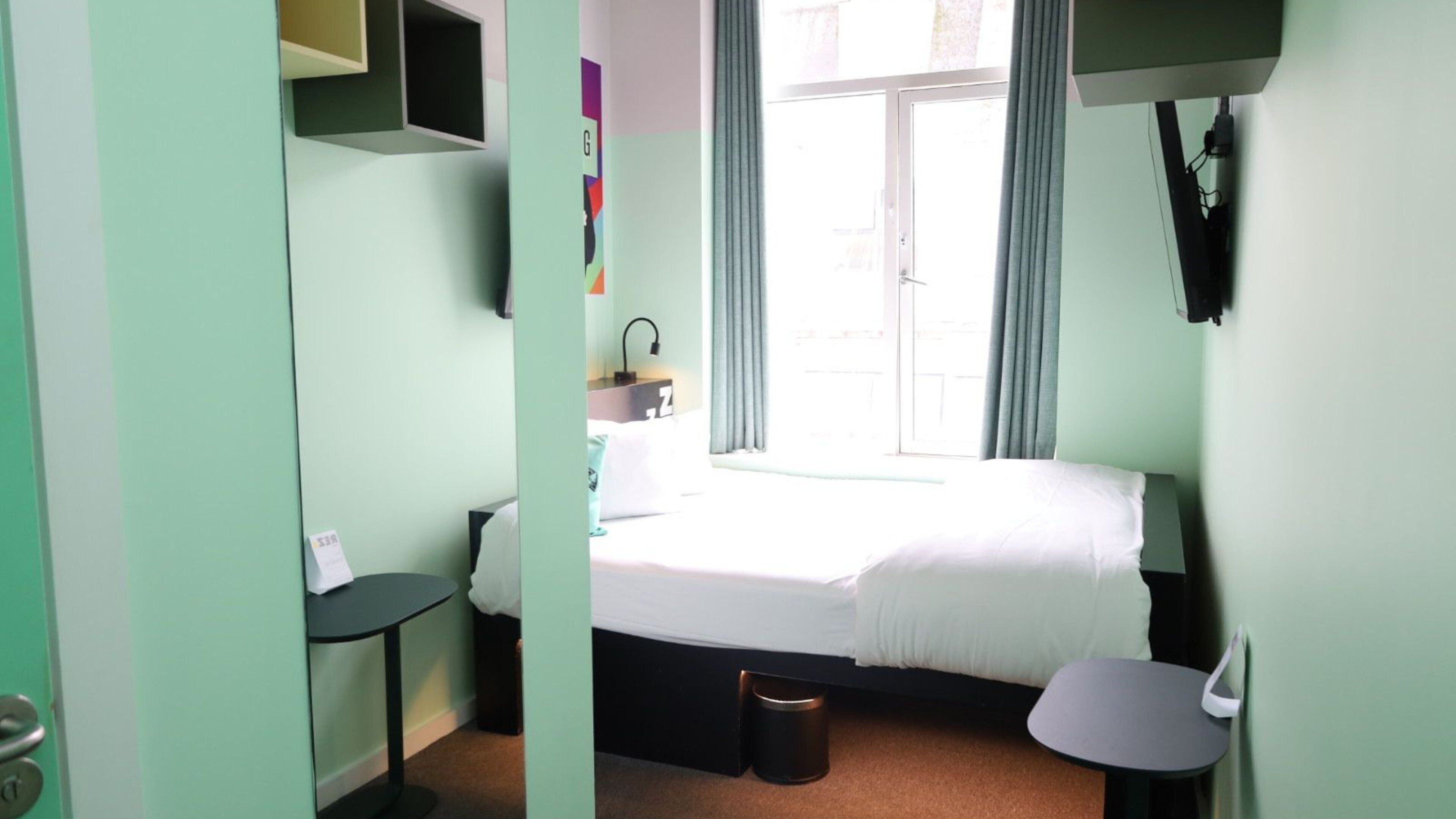 A room with a bed, a small table, a chair, a window with curtains, and a door.