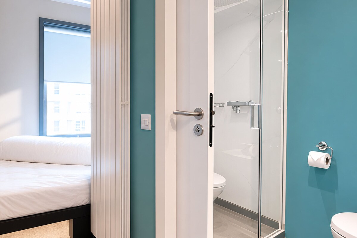 A modern hotel room with a bed, a shower, and a toilet.