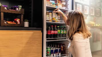 Una persona sistema oggetti in un frigorifero con ripiani pieni di bevande e snack assortiti.