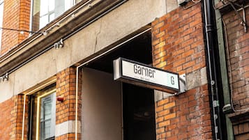 A street sign for 'Garnier' on a brick building with a window and a door.