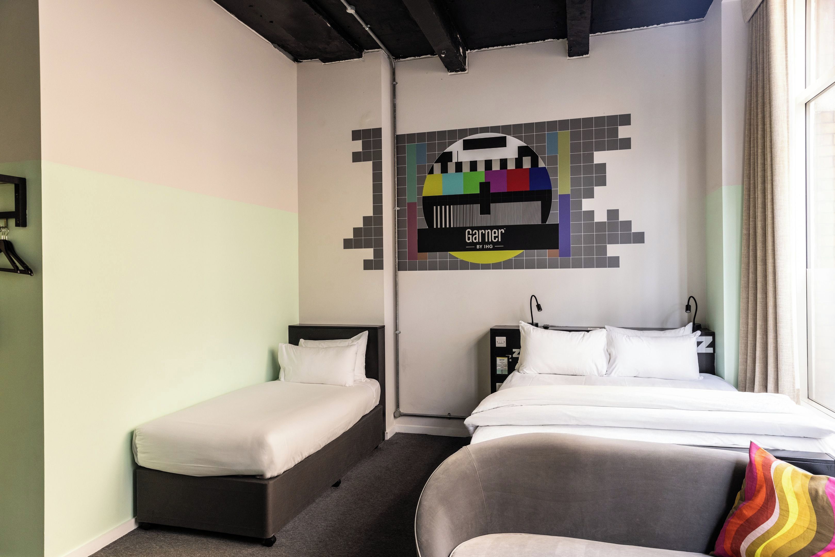 A hotel room with two single beds, a large bed, a wall-mounted TV, and a window with curtains.