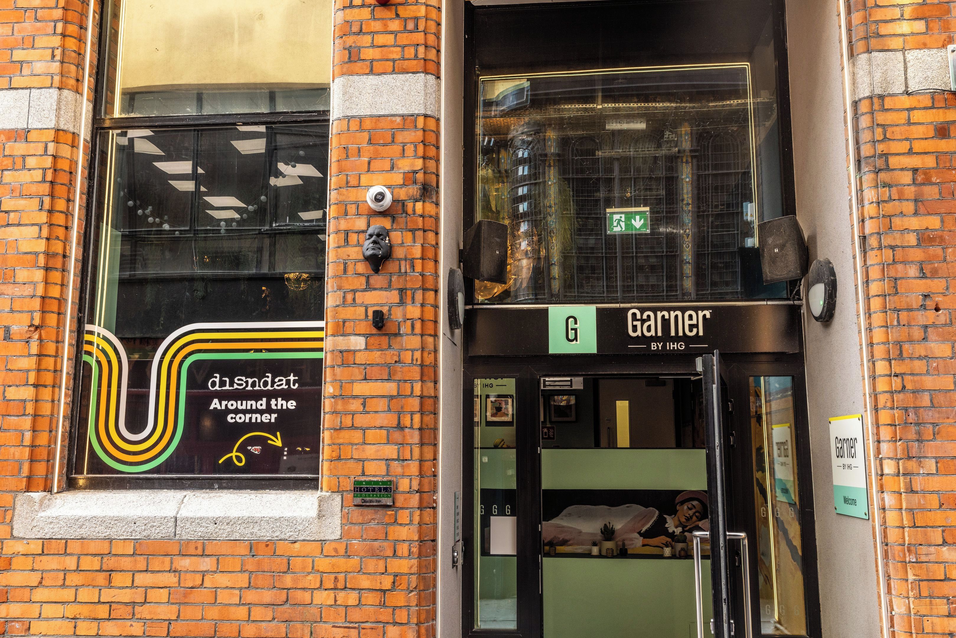 A hotel entrance with a sign for 'Garnier By IHG' and a window with a 'disndat Around the corner' sign.